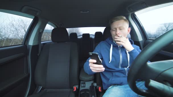 Trött ung man röka och använda smartphone i bilen i 4k — Stockvideo