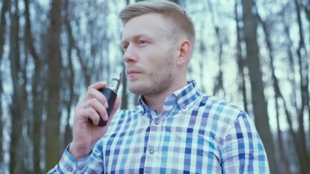Красивый элегантный мужчина курит электронную сигарету в лесу в 4K — стоковое видео