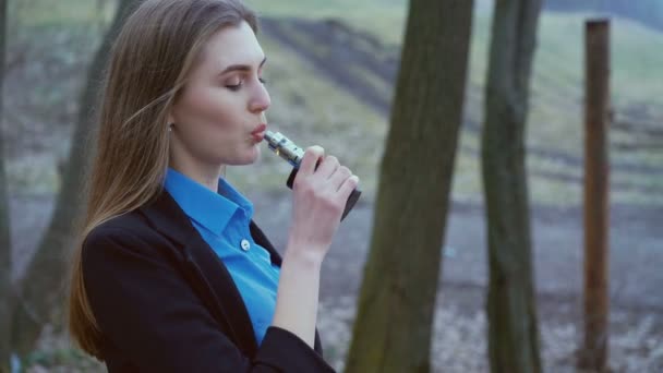 Mulher elegante inteligente fumando e-cigarro na floresta em 4K — Vídeo de Stock