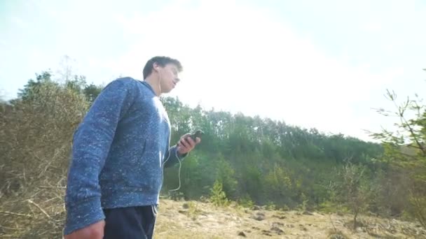 Jeune homme écoutant de la musique, utilisant un smartphone et marchant sur la nature 