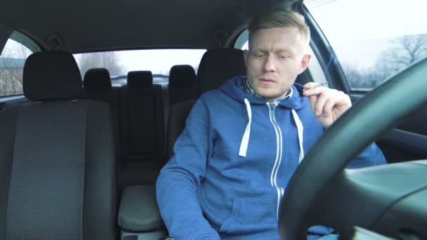 Hombre guapo sentado en el coche, fumando y hablando nerviosamente por teléfono — Vídeo de stock