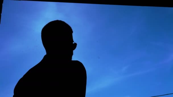 Black silhouette of man removing glasses on blue sky background 4K — Stock Video