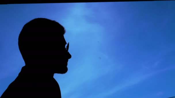 Черный силуэт человека, снимающего очки на фоне голубого неба 4К — стоковое видео