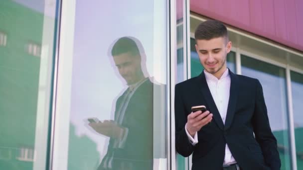 Красивый молодой человек с помощью мобильного телефона и улыбаясь на открытом воздухе в 4K — стоковое видео