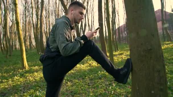 Молодой человек слушает музыку в наушниках и тренировки в раннем лесу 4K — стоковое видео