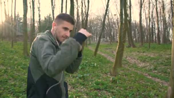 Joven escuchando música en auriculares y entrenamiento en el bosque temprano 4K — Vídeos de Stock