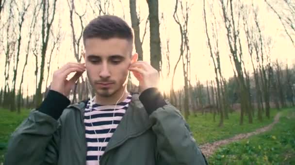 Jeune homme écoutant de la musique dans les écouteurs, marchant et se relaxant en forêt 4K — Video