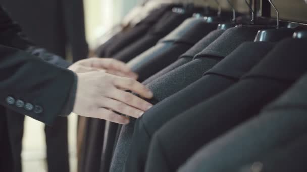 Elegante joven de traje escogiendo chaqueta en tienda de ropa — Vídeos de Stock