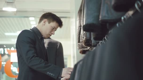 Elegant ung man i kostym att välja jacka i klädaffär — Stockvideo