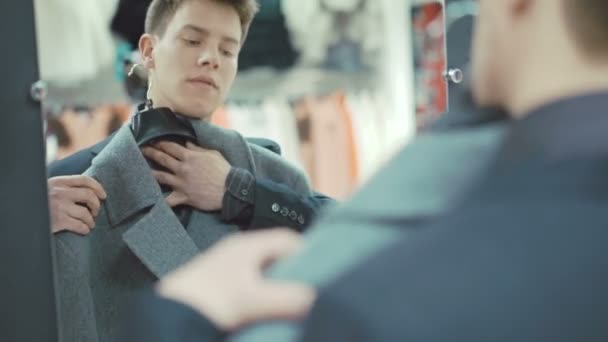 Элегантный молодой человек в костюме, примерка пальто в магазине одежды — стоковое видео