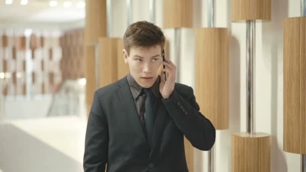 Hombre de negocios guapo haciendo una llamada telefónica con teléfono inteligente en el centro de comercio — Vídeos de Stock