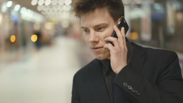 Guapo empresario exitoso haciendo una llamada telefónica en el centro de comercio — Vídeos de Stock