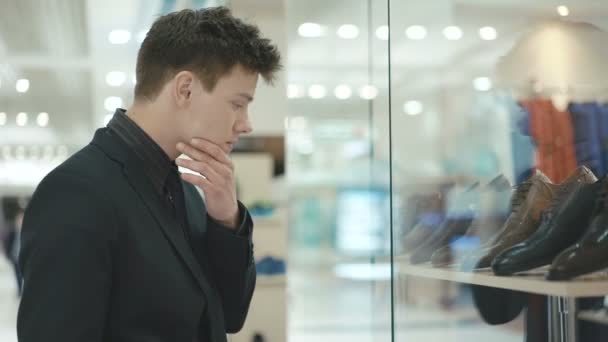 Hombre guapo de traje observa y duda en la compra de zapatos — Vídeo de stock