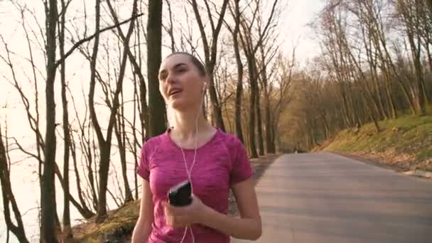 Bella ragazza che cammina nel parco e ascolta la musica in auricolare 4K — Video Stock