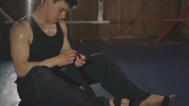 Masculino boxeador envolve suas mãos com bandagem preta no anel no ginásio — Vídeo de Stock