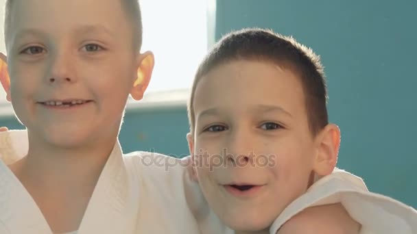 Dos divertidos chicos chipped abrazando, haciendo caras y riendo a la cámara en el gimnasio — Vídeos de Stock