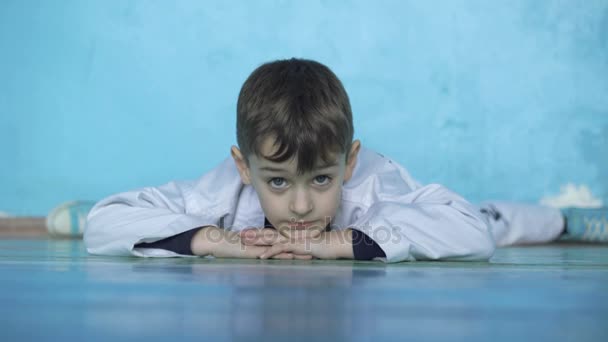 Retrato de niño divertido tirado en el suelo y se divide a la pared en el gimnasio 4K — Vídeos de Stock