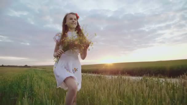 Junge süße Mädchen in Stickkleid springt in den Weizen mit Blumenstrauß — Stockvideo