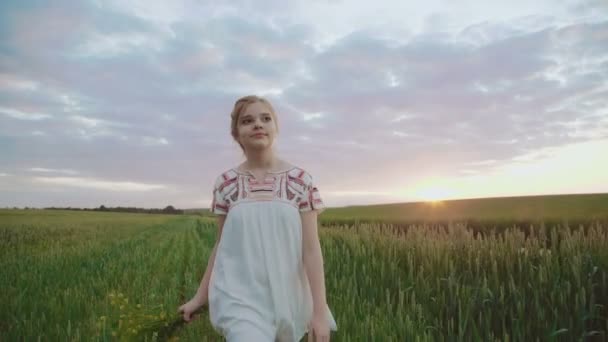 Schattig meisje in borduren jurk springt in de wheats met boeket bloemen — Stockvideo