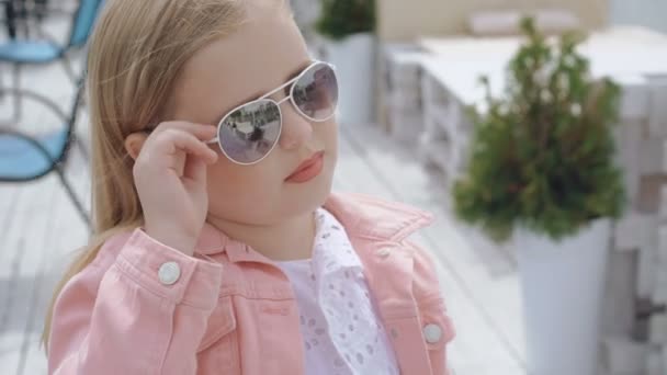 Petite blonde à la mode repousse les lunettes de soleil et regarde la caméra sur Bay Bar 4K — Video