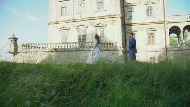Hochzeitspaar spaziert und Braut dreht Spinnerei in der Nähe des alten Schlosses — Stockvideo