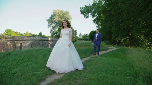 Hochzeitspaar spaziert und Braut dreht Spinnerei in der Nähe des alten Schlosses — Stockvideo