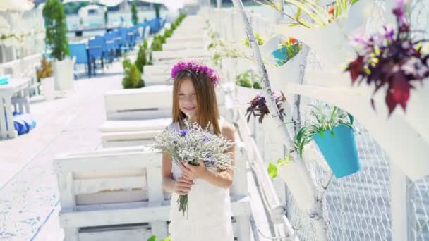 Gelukkig klein meisje met boeket bloemen glimlachend in de camera op de bay bar. 4k — Stockvideo