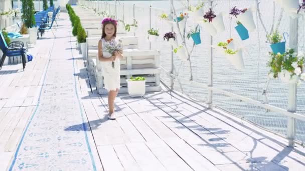 Niña feliz con ramo de flores camina a la cámara en el bar de la bahía. 4K — Vídeo de stock