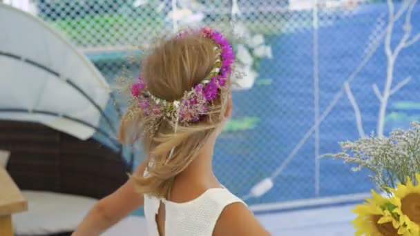 Liten blondin med blommor krona och blommor i händerna spinning på stranden 4k — Stockvideo