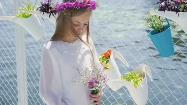 Милая девушка в белой вышивке с полевыми цветами в руках смотрит в камеру 4K — стоковое видео
