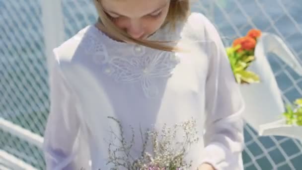 Schattig meisje in wit borduurwerk met wilde bloemen in handen kijkt camera 4k — Stockvideo