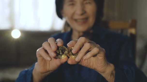 Portrait of old woman holds two golden bitcoins in hands at camera — Stock Video