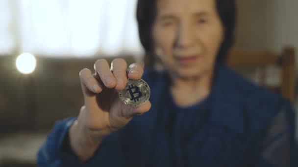 Portrait of old smiling woman holds a silver bitcoin in hand at camera — Stock Video