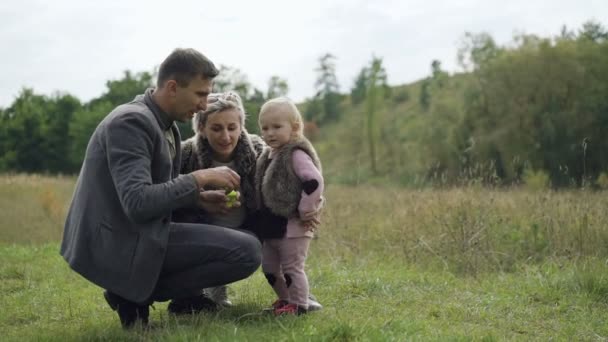 Feliz familia descansa en la naturaleza con el niño, soplando y atrapando burbujas — Vídeo de stock