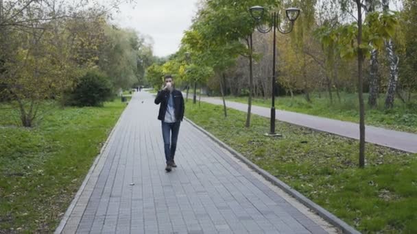 Όμορφος άνδρας περπατά σε Φθινοπωρινό πάρκο σοκάκι και πίνει καφέ 4k — Αρχείο Βίντεο