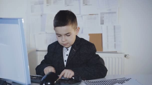 Kleiner gutaussehender Junge, der im Büro hart mit dem Computer arbeitet. 4k — Stockvideo
