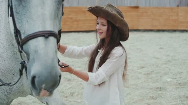 Jovem menina feliz sorrindo e acariciando seu cavalo branco bonito na área. 4K — Vídeo de Stock