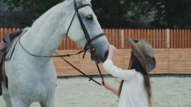 Genç mutlu kız gülümseyerek ve onun güzel beyaz atı alan üzerinde okşama. 4k