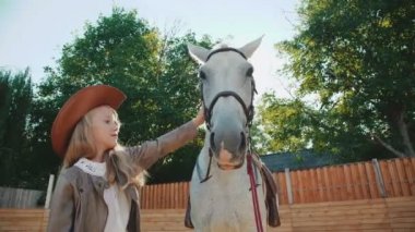 Dokunmaktan ve alan üzerinde beyaz bir at sevecen küçük kız. 4k