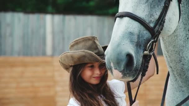 Jovem menina feliz acariciando seu cavalo branco bonito na área. 4K — Vídeo de Stock