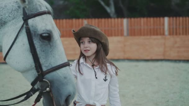 Retrato de una niña feliz acariciando bonito caballo blanco en la zona. 4K — Vídeo de stock