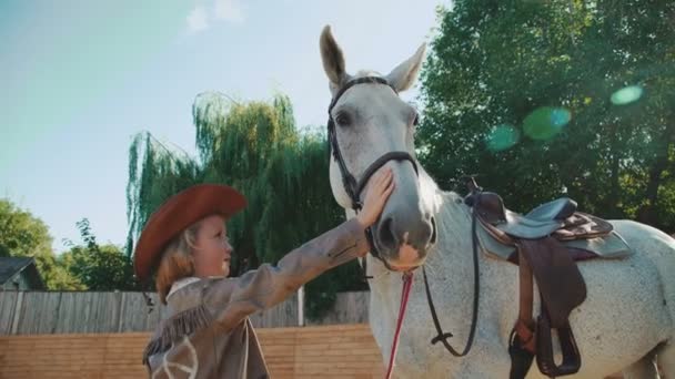 Ragazza felice sorridente e accarezzando un cavallo bianco sulla zona. 4K — Video Stock