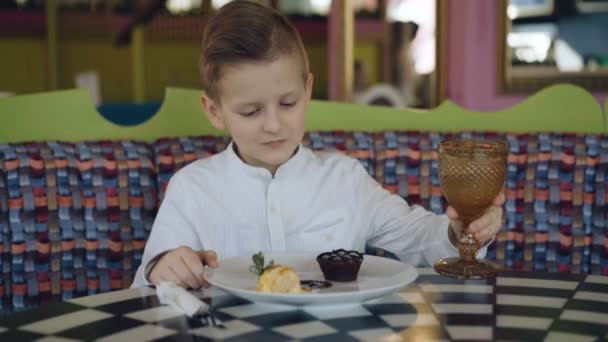 Menino bonito bebe, acena com a cabeça e começa a comer uma sobremesa — Vídeo de Stock