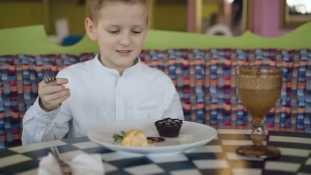 Guapo niño sonriente comienza a comer un sabroso postre en la cafetería. 4K — Vídeos de Stock