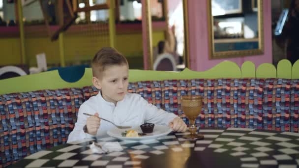 Όμορφος χαμογελαστό αγόρι τρώει ένα νόστιμο επιδόρπιο και κουνώντας το κεφάλι στο καφέ — Αρχείο Βίντεο