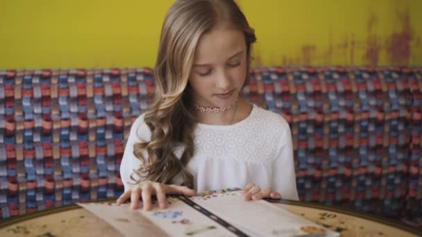 Chica bonita, sonriente y joven leyendo el menú en la cafetería. 4K — Vídeo de stock