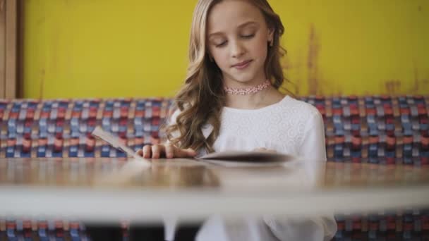 Hezká, usměvavá a mladá dívka, čtoucí menu v kavárně. 4k — Stock video