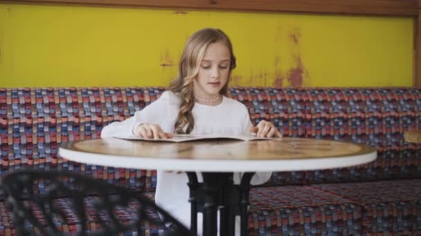 Hezká, usměvavá a mladá dívka, čtoucí menu v kavárně. 4k — Stock video