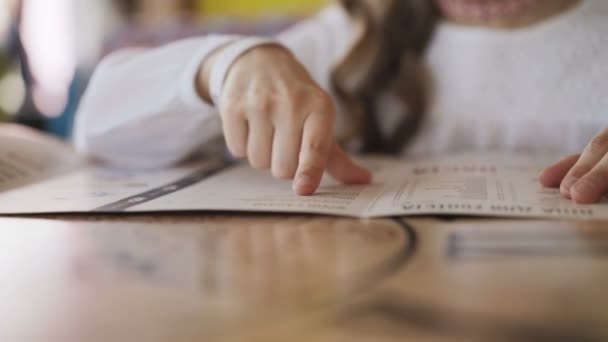 Unrecognizable young girl leads the finger on the menu in cafe. 4K — Stock Video