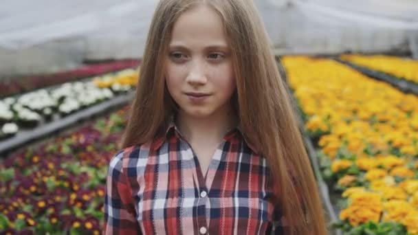 Portret van gelukkig jong meisje ruikende bloemen in de serre aan de camera — Stockvideo